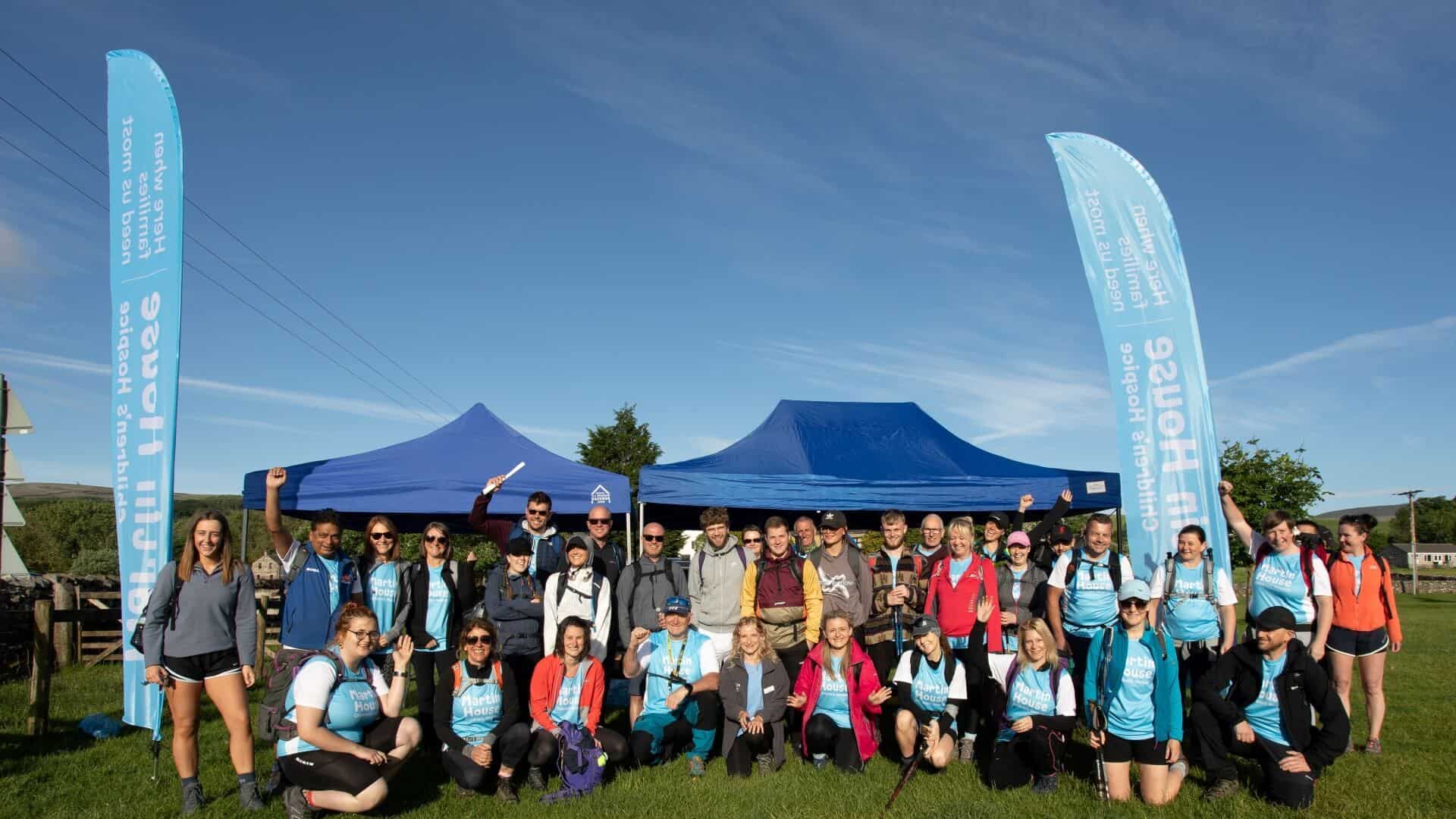 Large group of people stood under gazebo on sunny day.