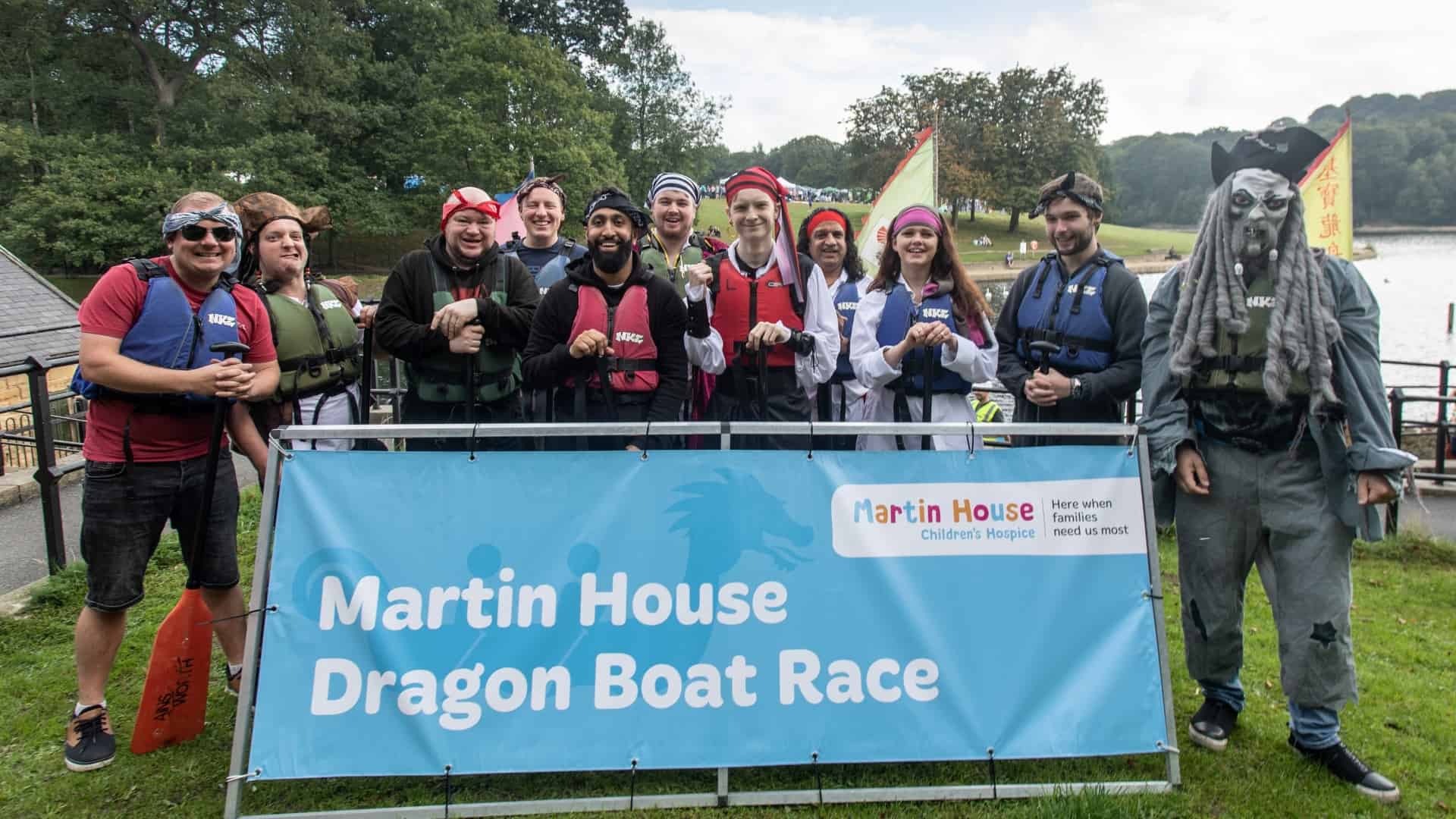 Group of people in fancy dressed holding sign saying Martin House Dragon Boat Race