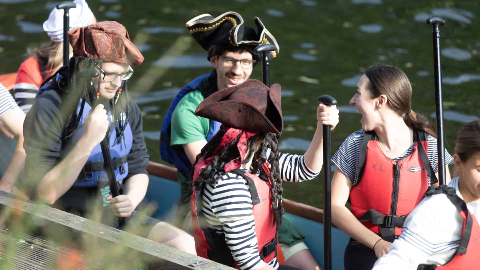 Group of people in fancy dress in a boat on a lake.