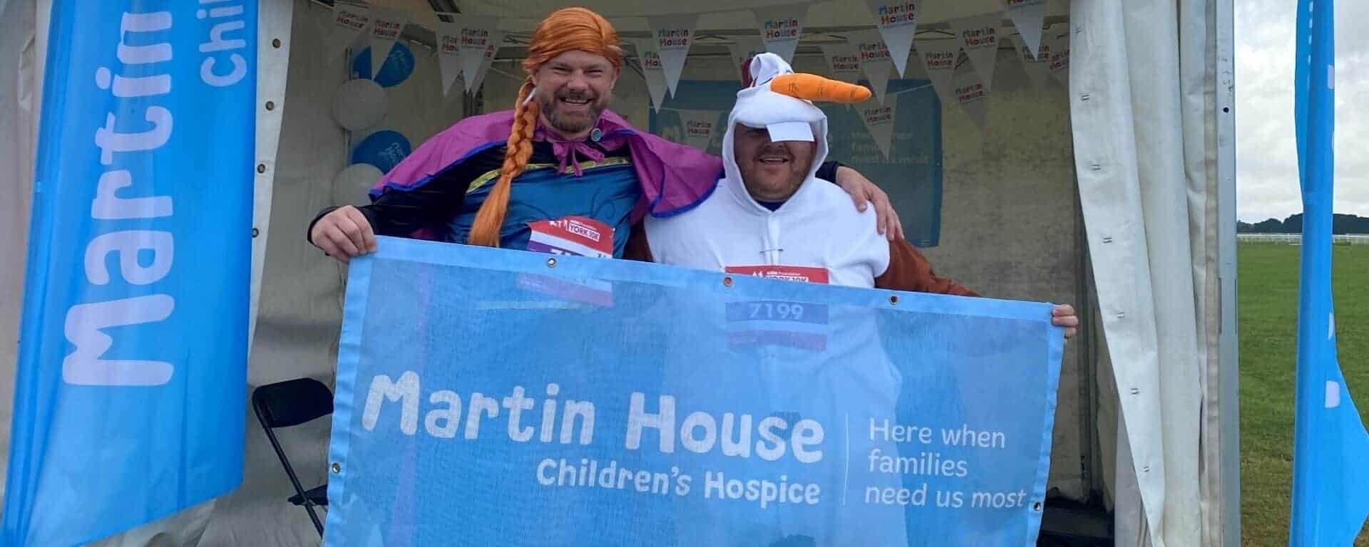 Two men dressed as Anna and Olaf from Frozen with Martin House sign.