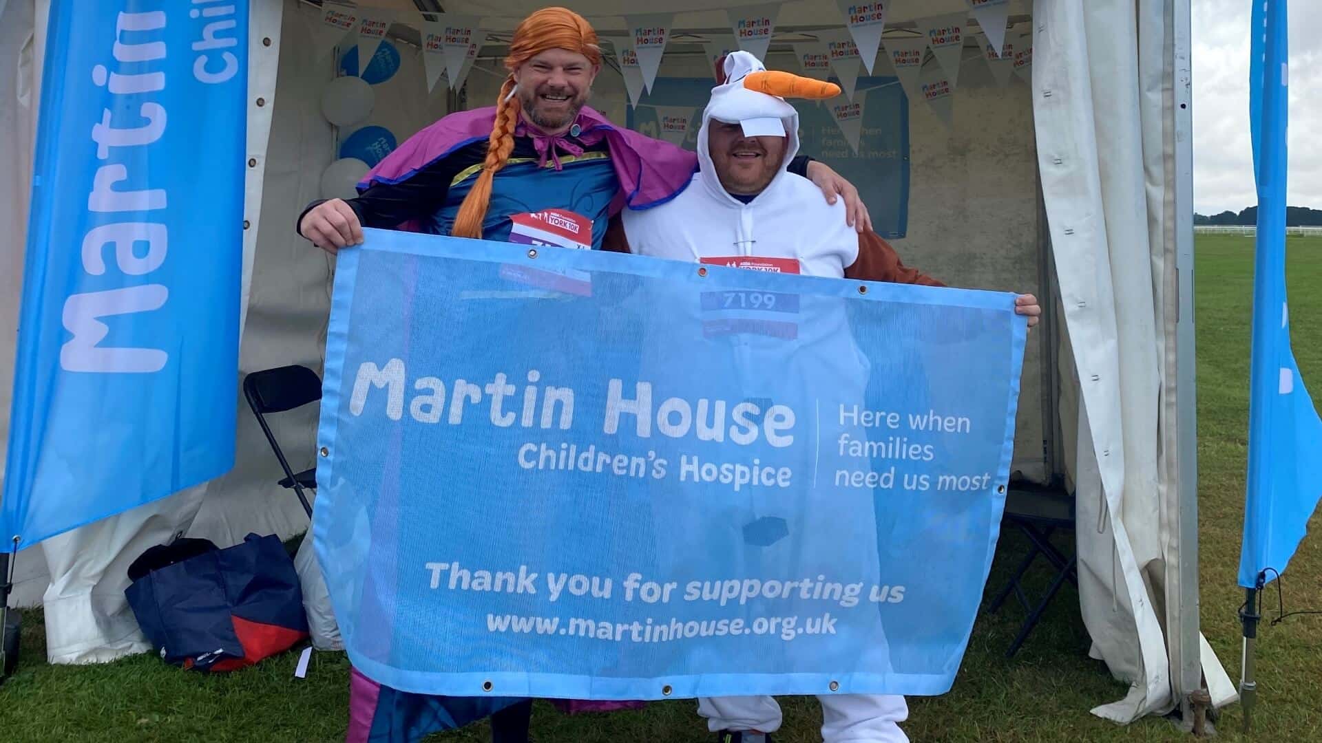 Two men dressed as Anna and Olaf from Frozen with Martin House sign.