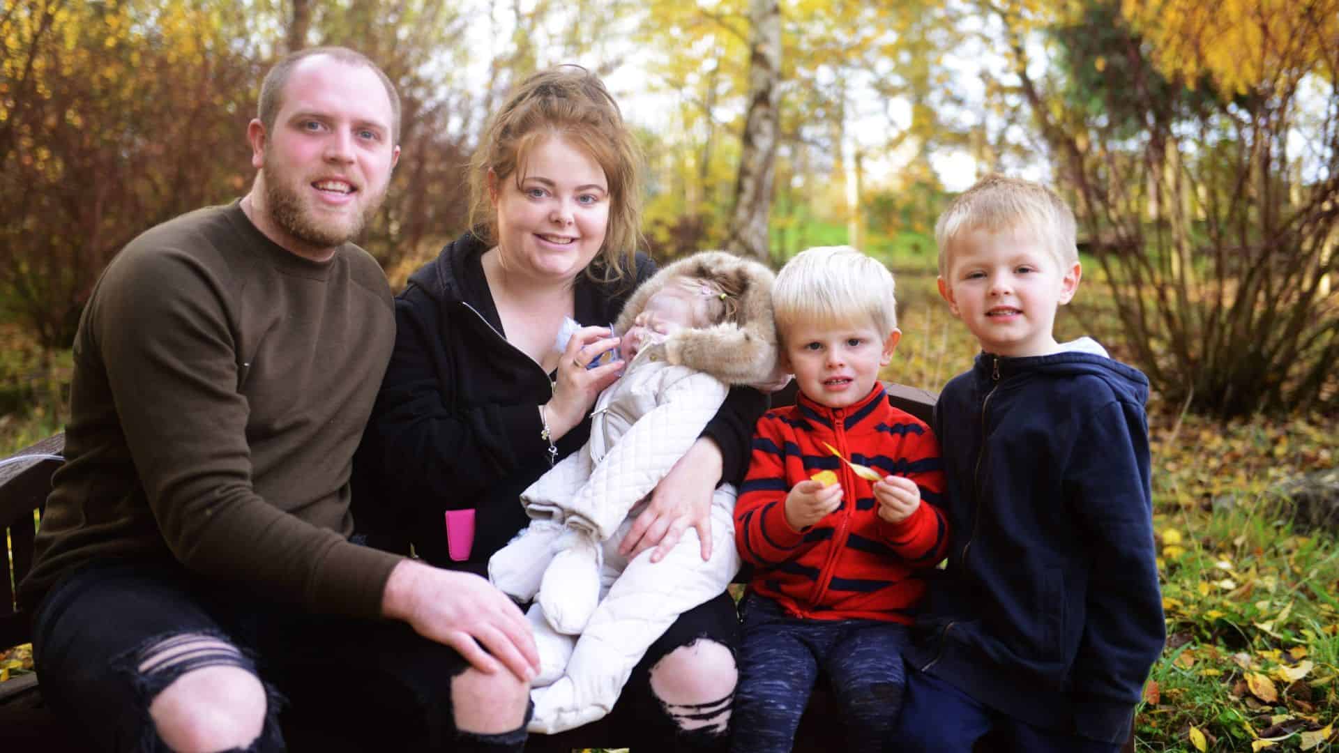 Family stood in woodland area with two young children, mum, dad and baby.