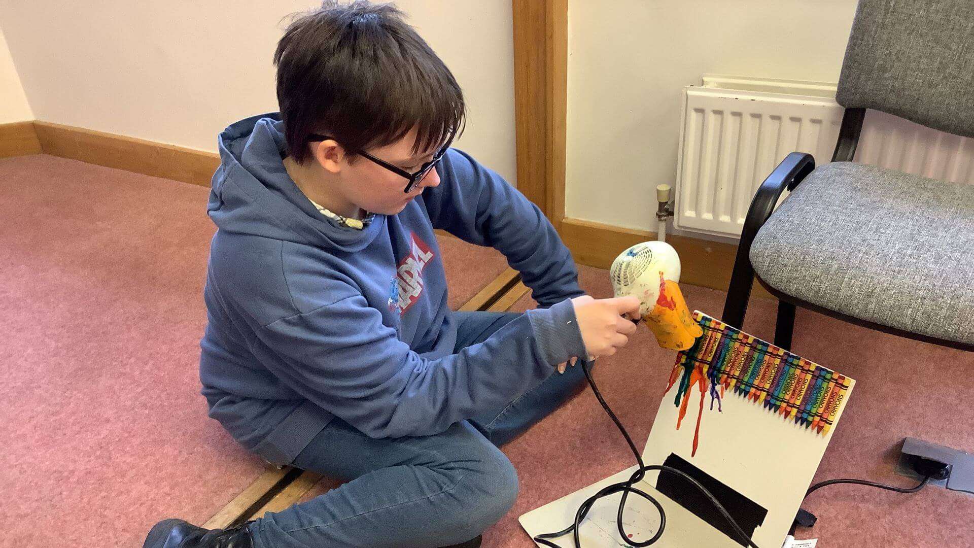 Child using a hairdyer to melt crayons for art.