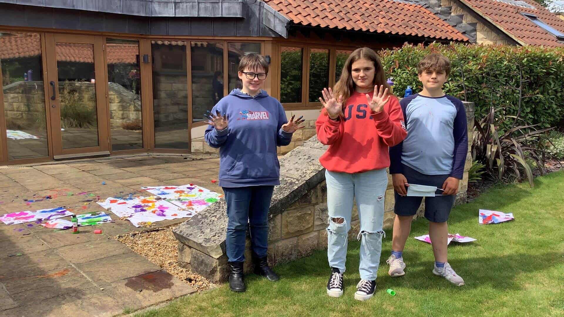 Three children waving their hands with their art work