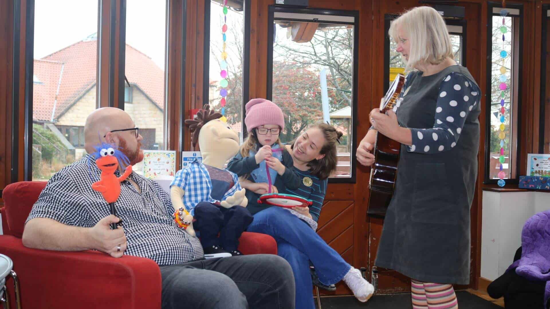 Family sat on sofa singing with music therapist with guitar