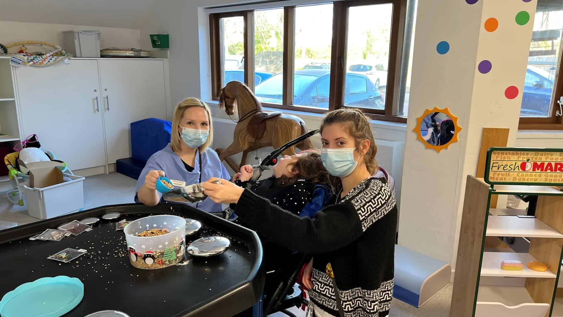 Two members of care team doing sensory play with young child.