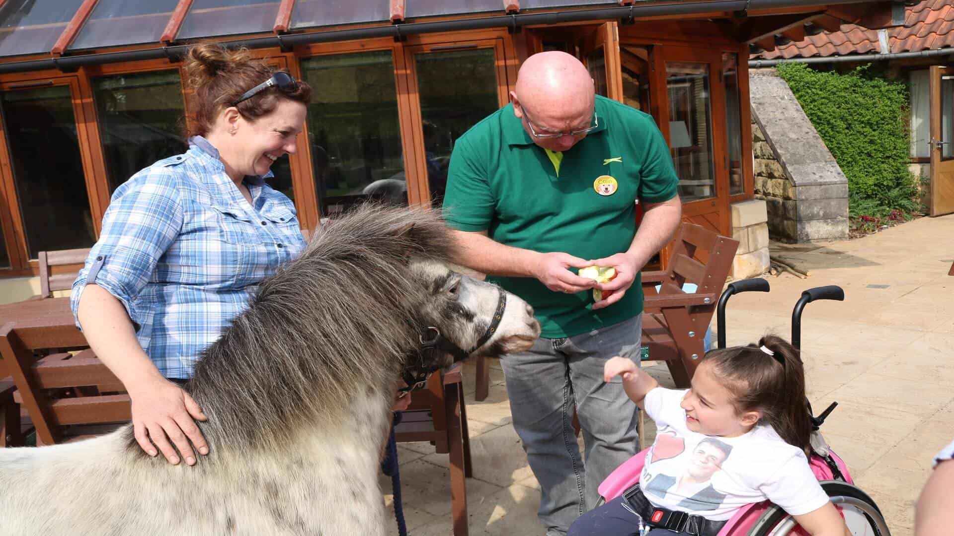 Man and women with young girl stroking a pony.