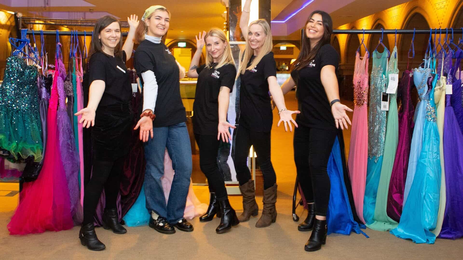 Five women stood between rails of dance dresses