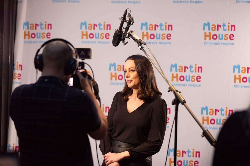 Woman behind a camera being interviewed in front of Martin House back drop