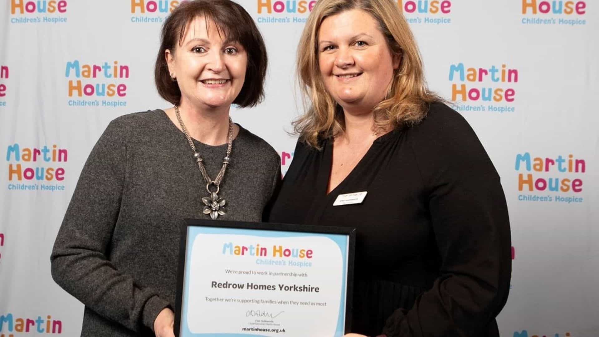 Two women holding partnerships certificate for Redrow homes Yorkshire