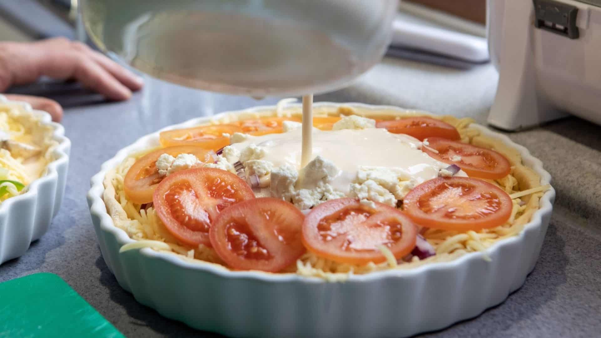 Quiche in a dish with cream being poured on top.