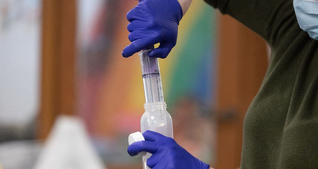 Hands wearing medical gloves measuring out medicine.