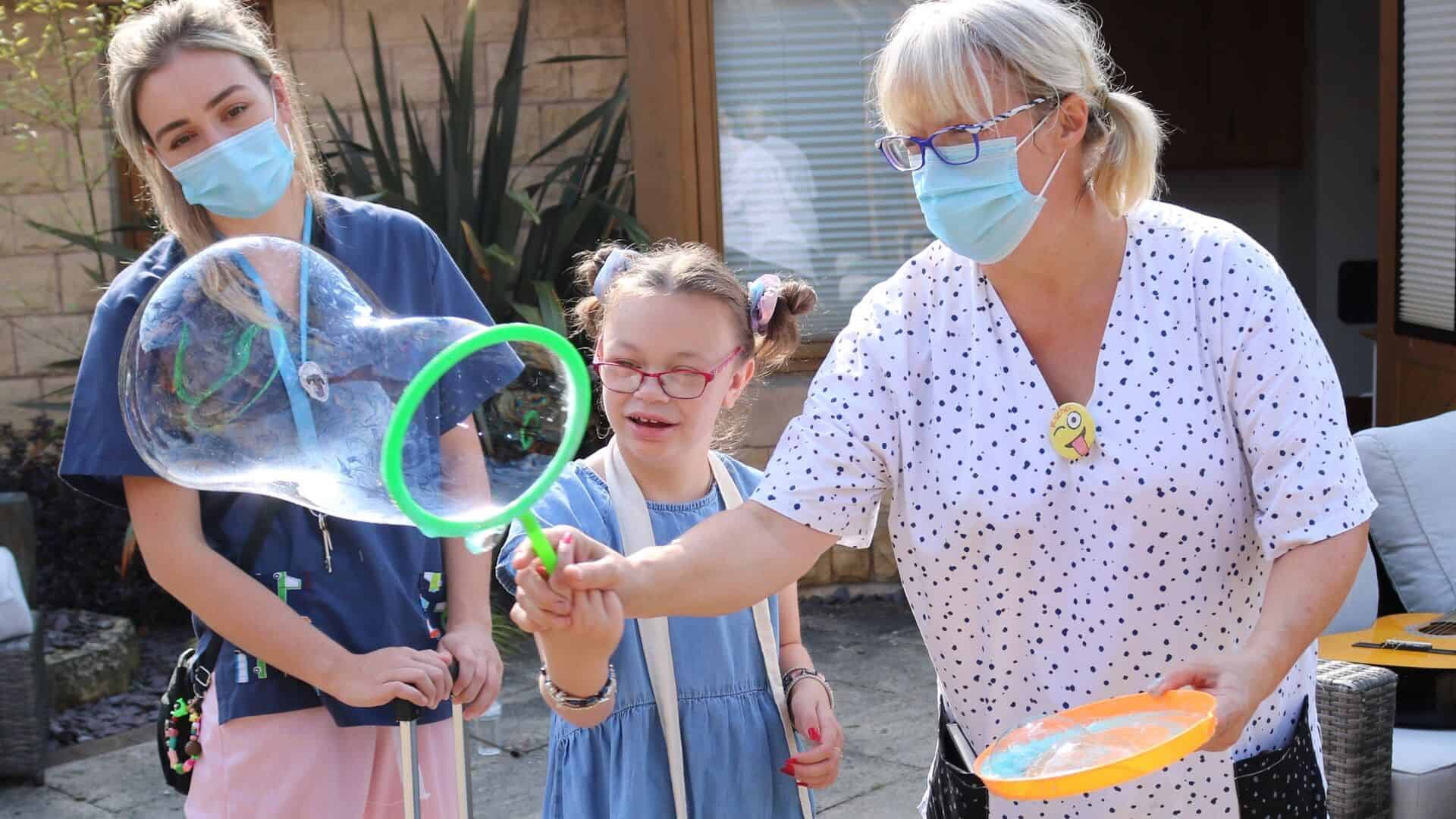 Two women blowing bubbles with young girl.