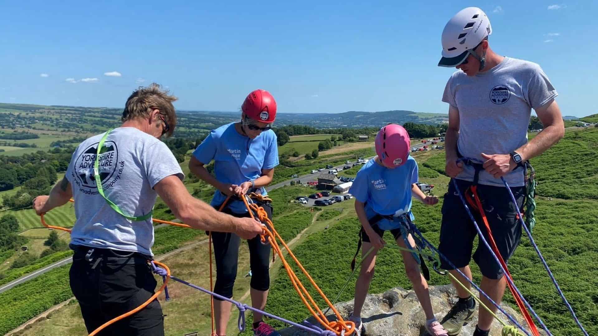 Four people wearing helmets attached to ropes preparing to abseil