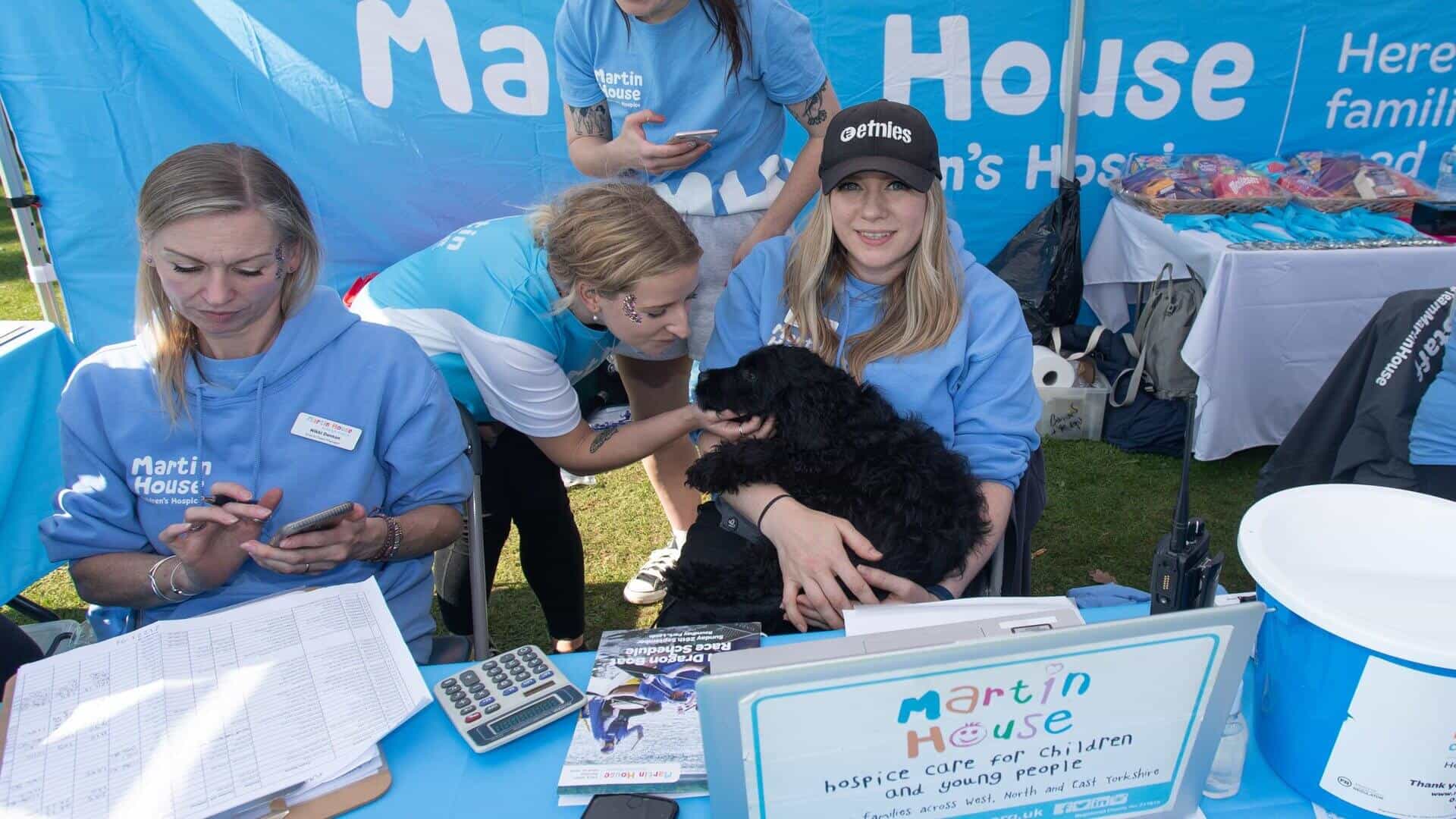 Three women sitting with a black dog with Martin House backdrop