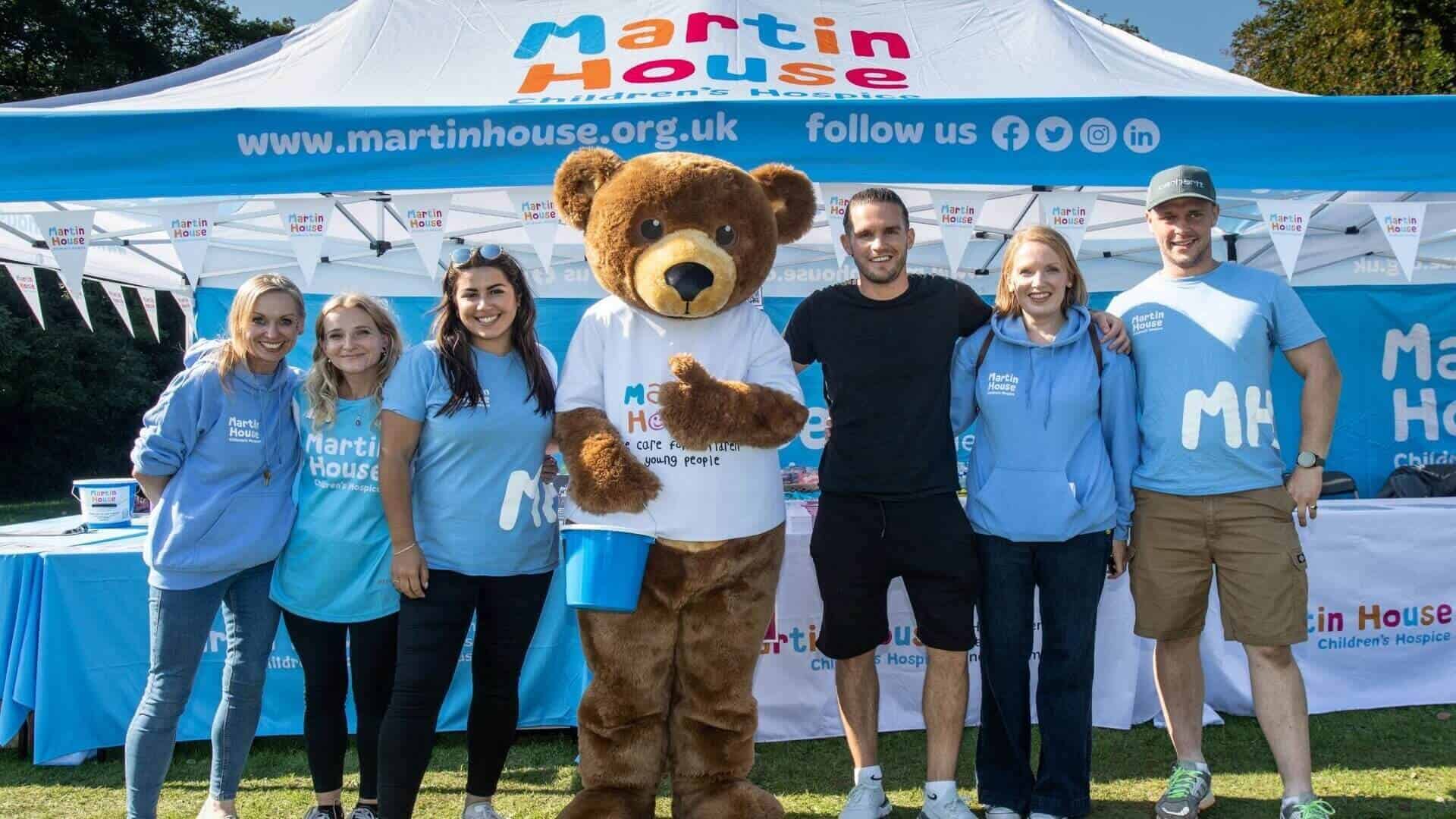 Six people stood by Martin House gazebo with teddy bear mascot in the middle.