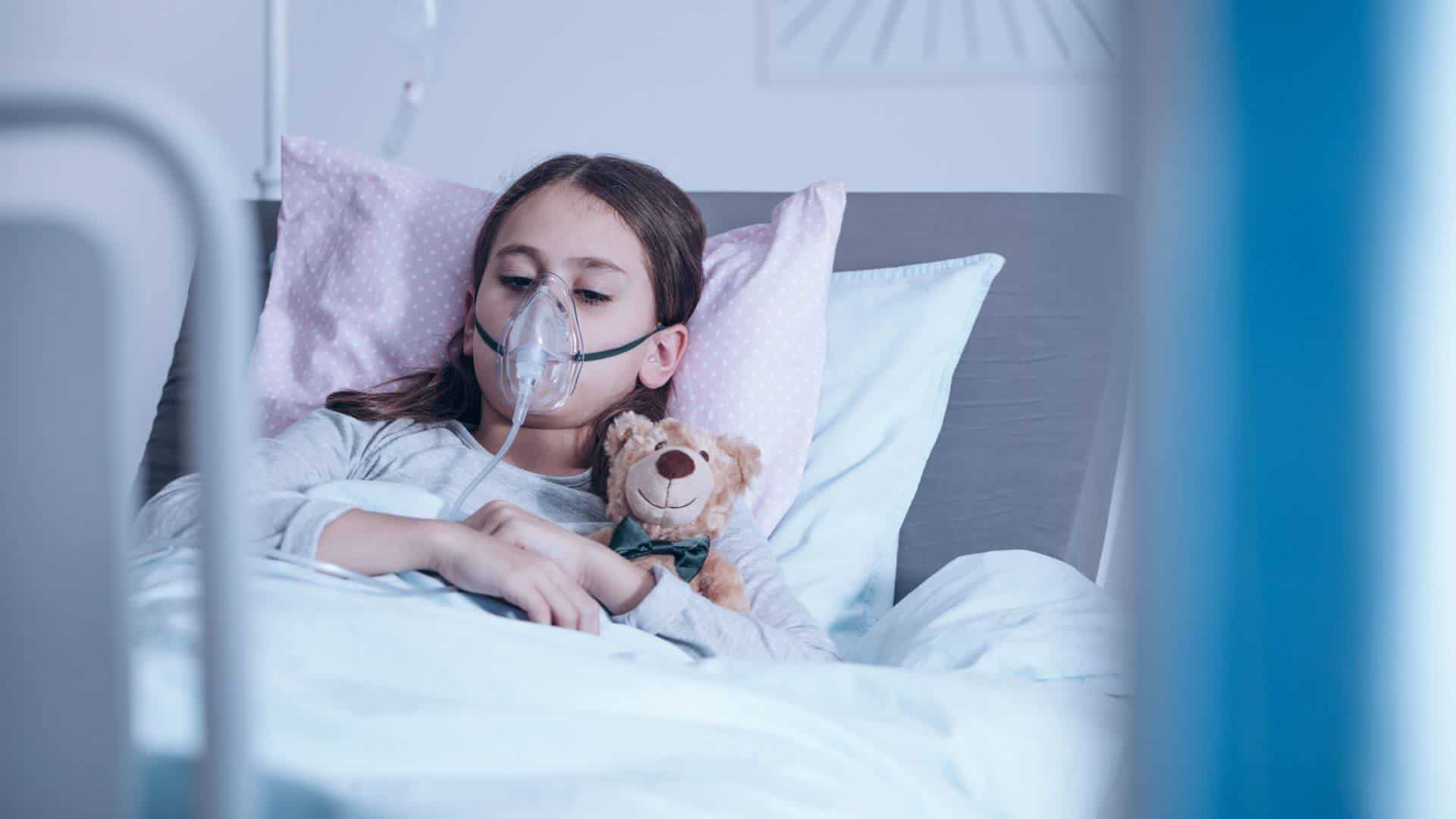 Girl in hospital bed with soft toy teddy bear.