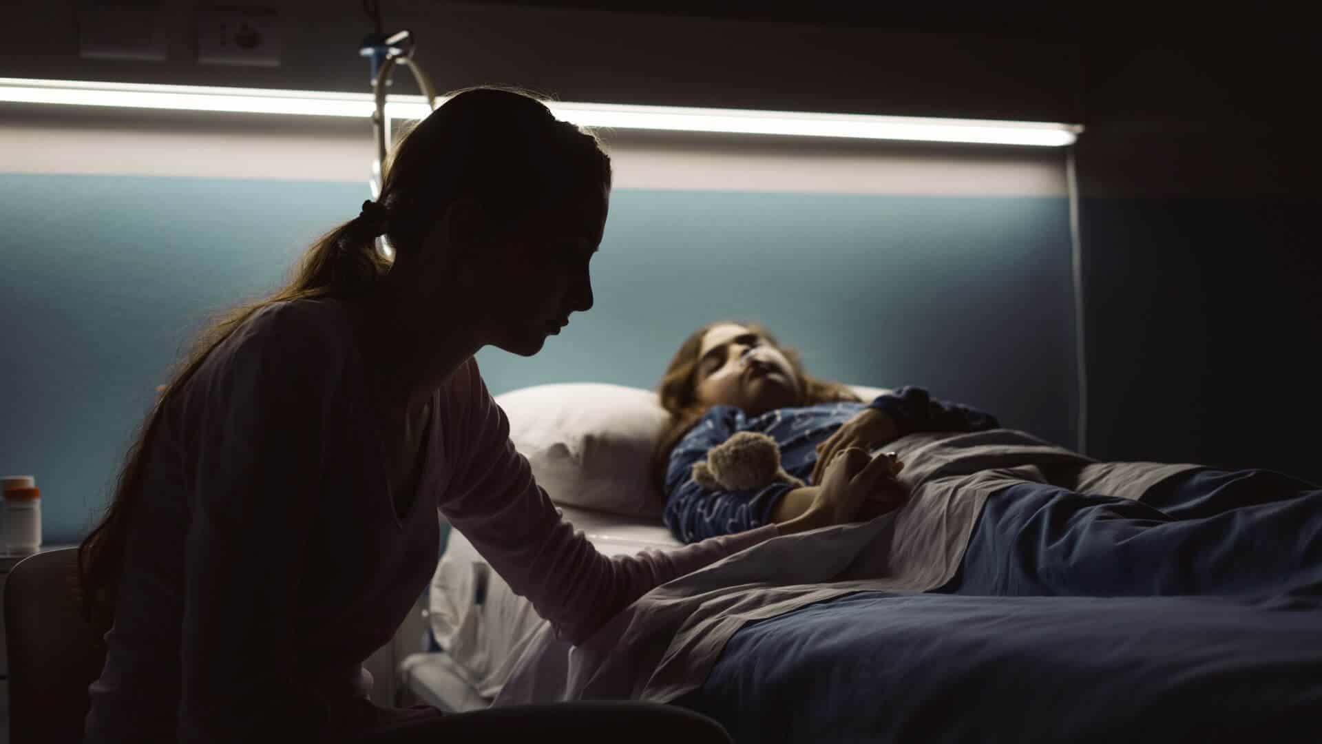 Woman looking over child in bed with teddy.