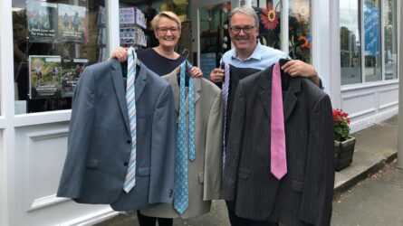 Man and woman holding up three suits and ties outside Martin House shop