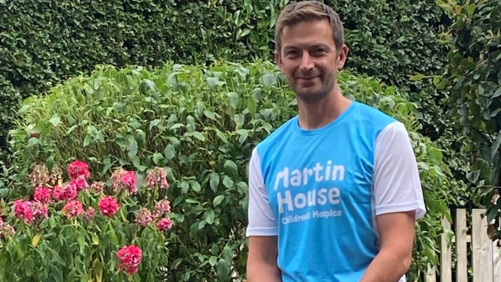 Sam Yates sat in garden wearing blue Martin House branded t-shirt.