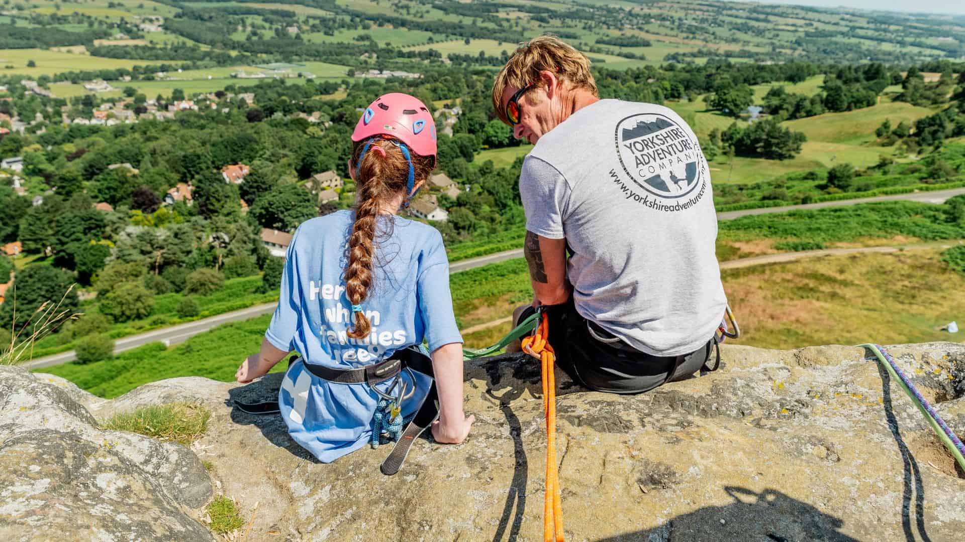 Young girl and man from Yorkshire Adventure Company sat at top of Cow and Calf ready to abseil down.