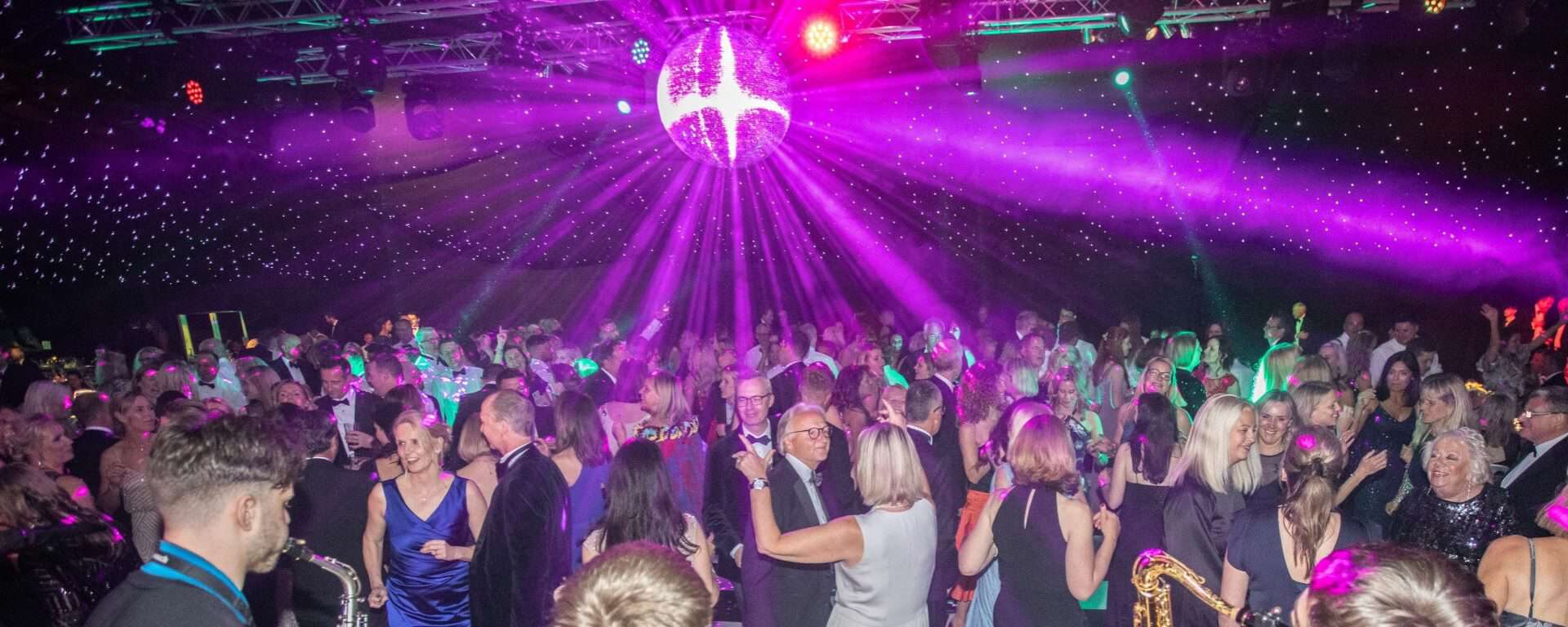 People dancing to a live band under Glitter Ball and disco lights.