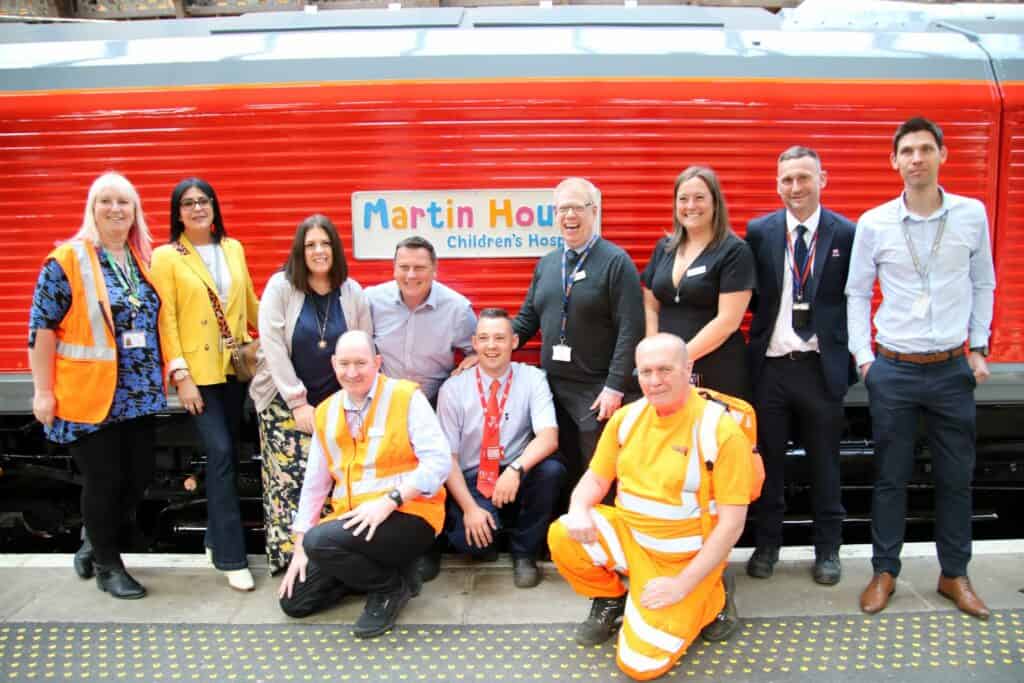 The charter train charity fundraising team gather in front of the locomotive with the Martin House Children's Hospice logo.