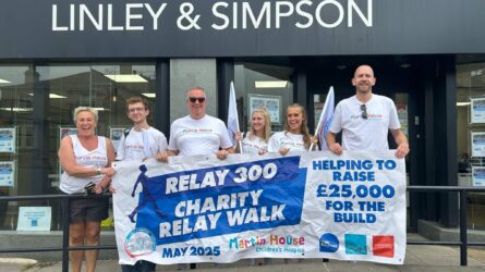A group of six people stand smiling in front of a Linley & Simpson storefront, holding a banner that reads "RELAY 300 CHARITY RELAY WALK MAY 2025" and "HELPING TO RAISE £25,000 FOR THE BUILD." They are wearing white Martin House Children's Hospice t-shirts. The banner includes logos for Martin House, Dale Eddison, Linley & Simpson, and Hardisty.